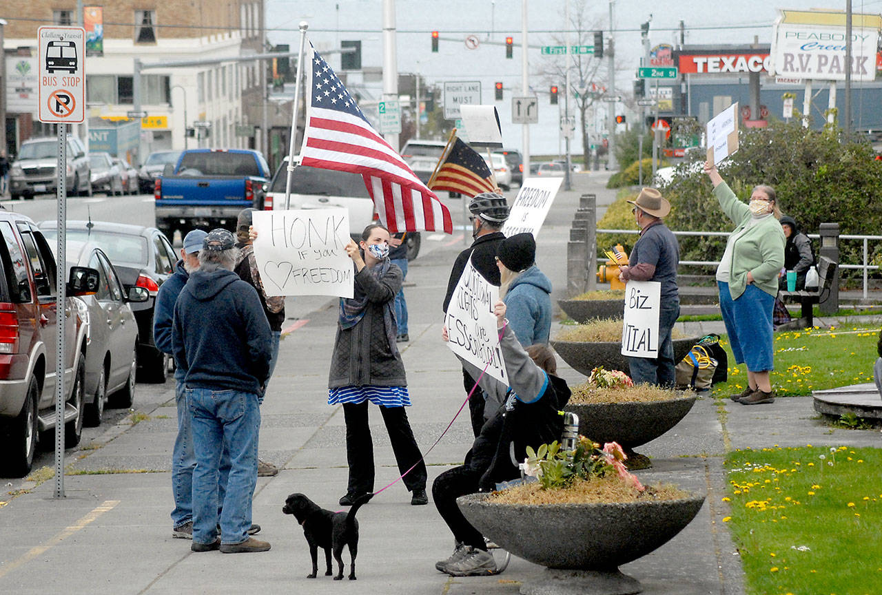 A group of about a dozen people against the state’s stay-at-home directives to combat spread of COVID-19 wave signs and flags at a gathering Thursday, April 23, 2020, at Veteran’s Park in Port Angeles. (Keith Thorpe/Peninsula Daily News)