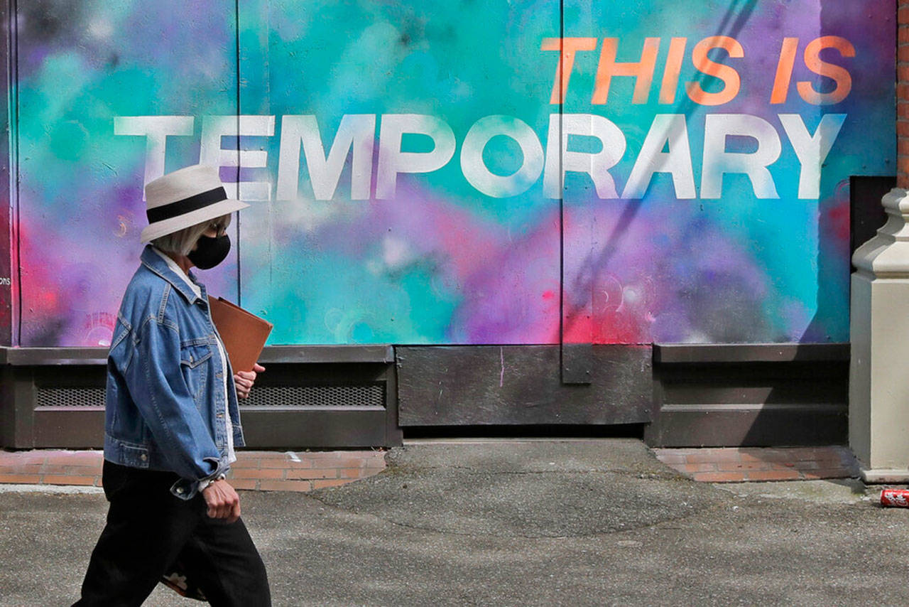 A person wearing a mask walks past a mural on a boarded-up window that reads “This is temporary,” on Tuesday, April 28, 2020, in Seattle. Public street art has sprung up all over the city as businesses closed to prevent the spread of the coronavirus or due to government stay-at-home orders have temporarily boarded up their windows. (Ted S. Warren/Associated Press)