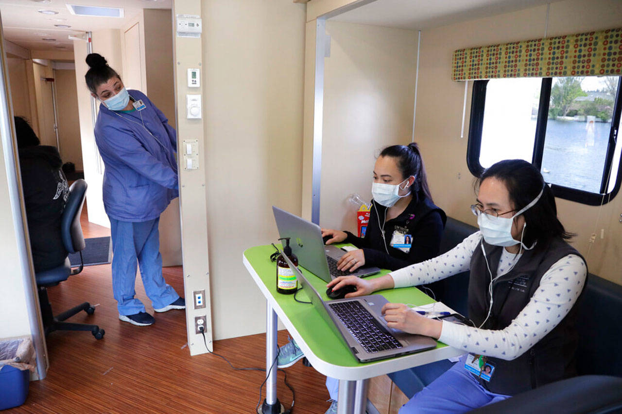 Sarah VanBuskirk, left, looks across to talk with fellow patient service specialists Yuehua Liang, right, and Eva Villanueva as they prepare records via cell phone for patients driving up to a coronavirus testing site Wednesday, April 29, 2020, in Seattle. The site, open Wednesdays and Saturdays from 10 a.m. to 3 p.m. in the Rainier Beach neighborhood, is available to anyone displaying the virus symptoms, are pregnant, over 60 or have a chronic condition, as well as health care workers and first responders. (Elaine Thompson/Associated Press)
