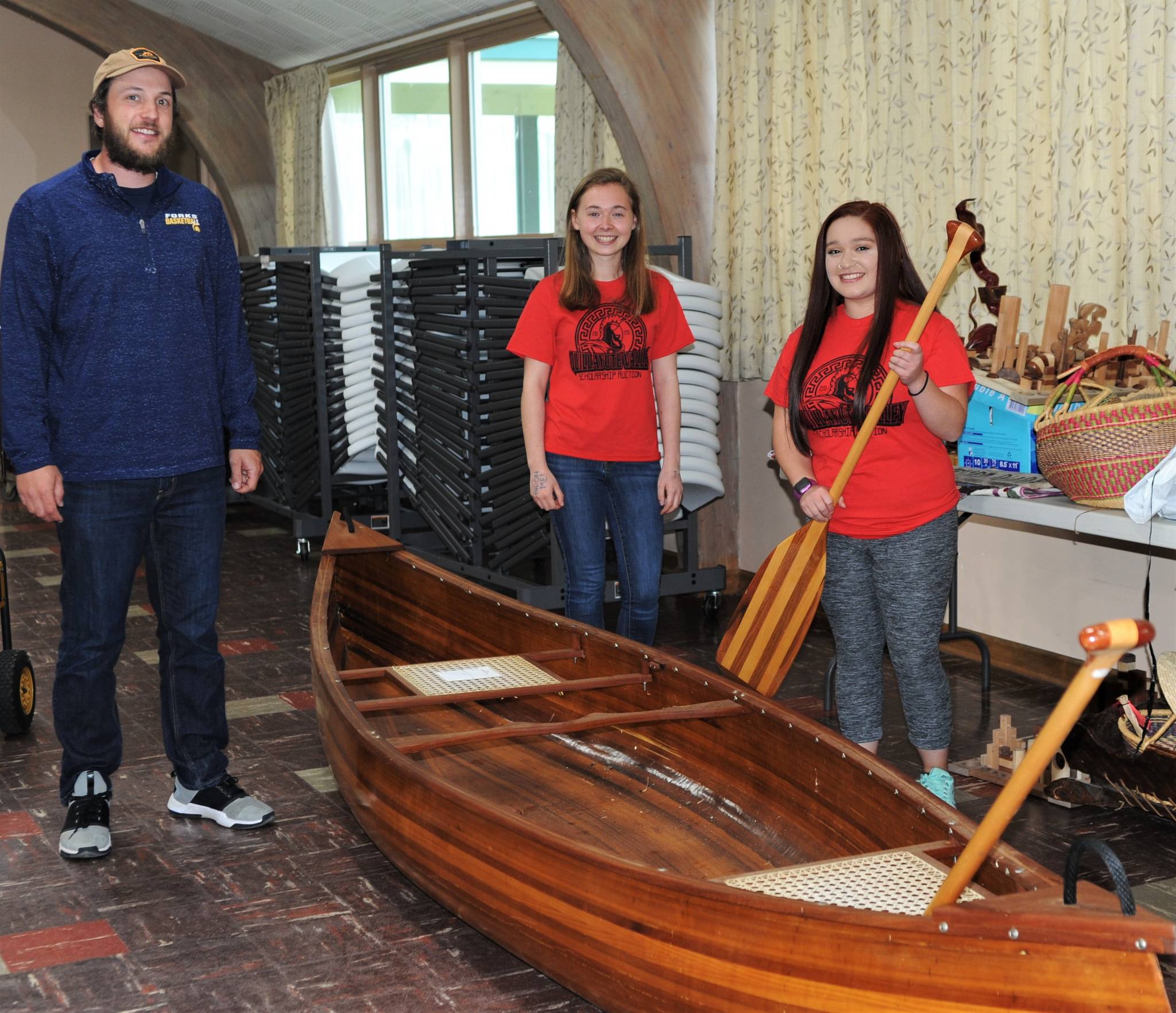 QVSA organizer David Hurn and student Scholarship Auction coordinators, Madelyn Archibald and Olivia Gonzalez gather around a custom-built wooden canoe donated by Rich McMenamin Saturday during the auction. Photo by Lonnie Archibald