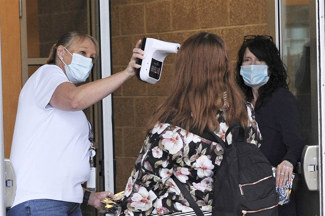 Connie Munson (left) and Tina Hagen take temperatures and hand out masks to students as they enter FHS Monday, Oct. 5 for the first day of school.