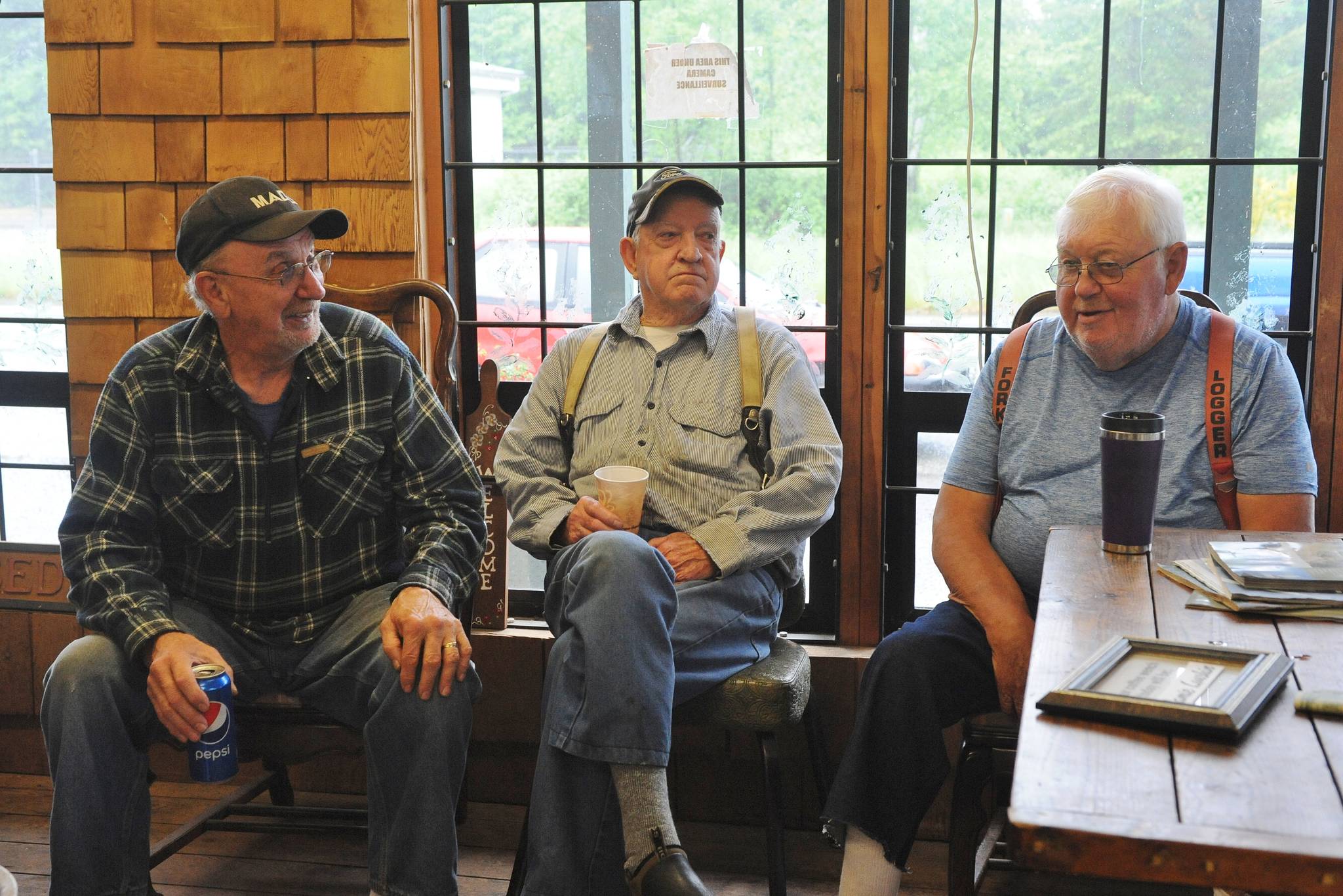 Richard Halverson, Pioneer Logger 2019, with Jack Banner, and Dean Hurn, on the right, Pioneer Logger Award winner for 2020. This photo was taken by Lonnie Archibald during past coffee hours at the Lake Pleasant Grocery where truckers, loggers, fishermen, mill rites, etc. once met to discuss important things.