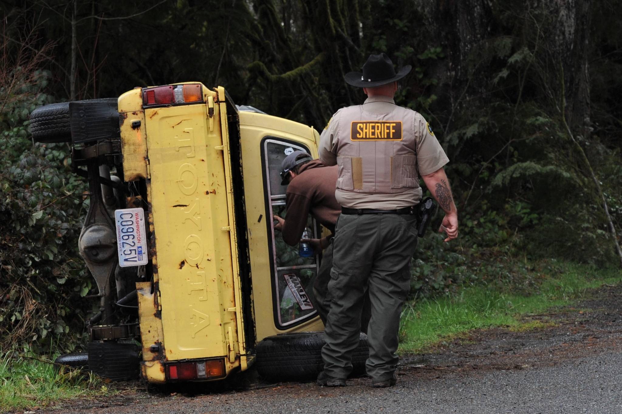 A Clallam County Sheriff deputy inspects the scene of a Toyota pickup which ended on its side at the Junction of Highway 101 and Shuwah Road at approximately 3 p.m. Wednesday March 24. Also responding were Fire district 1, Forks police, and the Forks Ambulance crew. Photo by Lonnie Archibald