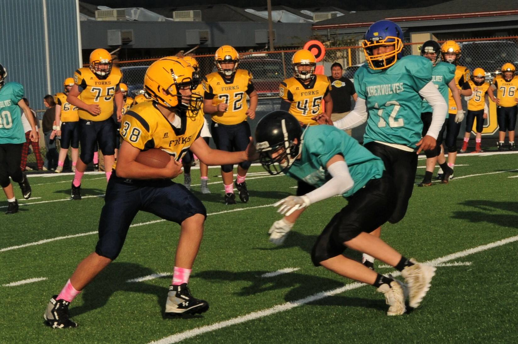 At right: Spartan Kade Highfield (38) carries the ball against Sequim defenders. Also in the action are Spartans Kenny Daman (75), Carter Coberley (72), and Carlos Soto (45).