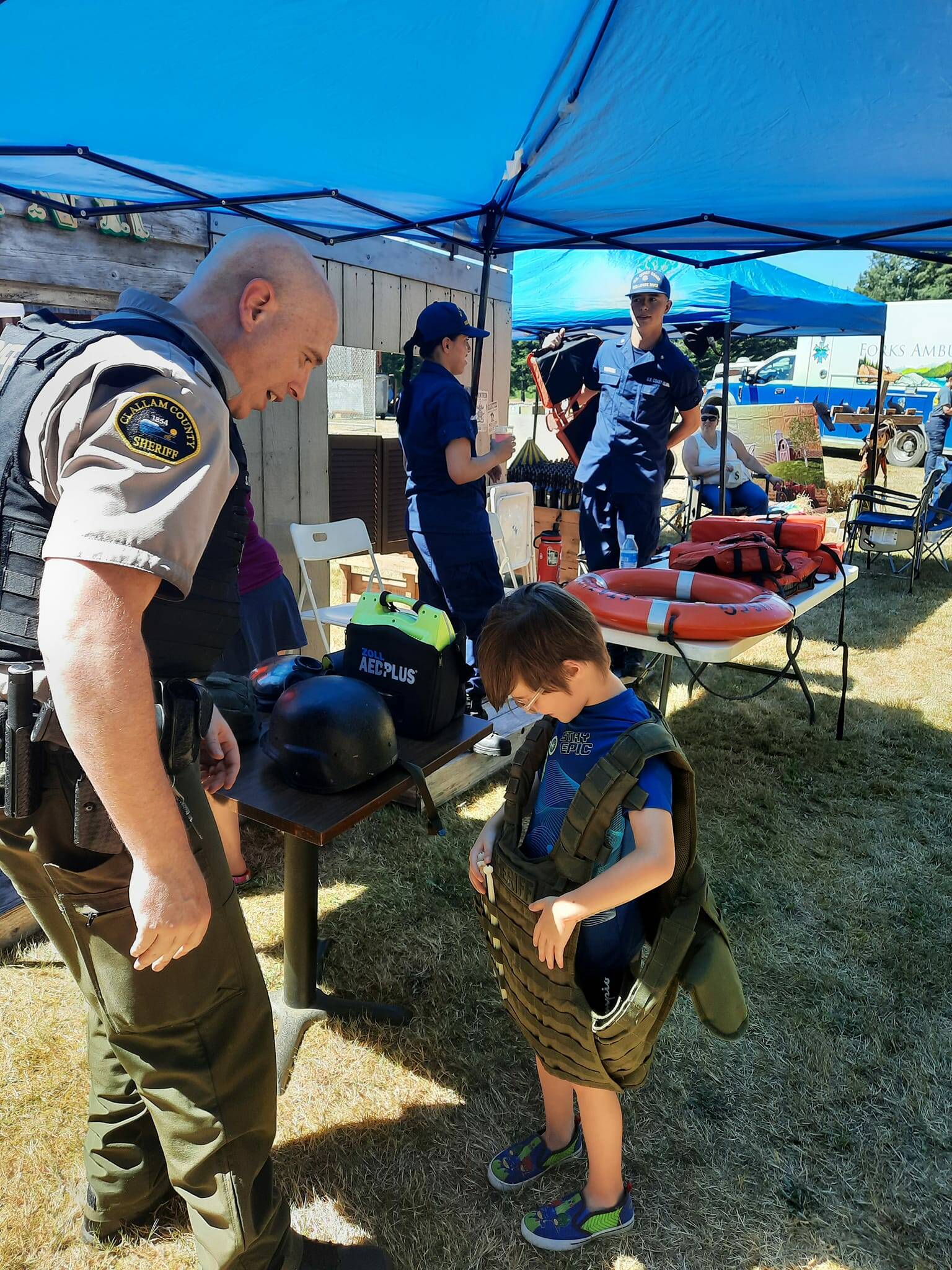 Sean Hoban with the Clallam County Sheriff’s Office offered a vest demonstration to those that wanted to try it on. Hoban was also strategically placed next to the Bank and the Jail.
 USCG Station Quillayute River members, seen in the background, also participated, with a lifevest demonstration.