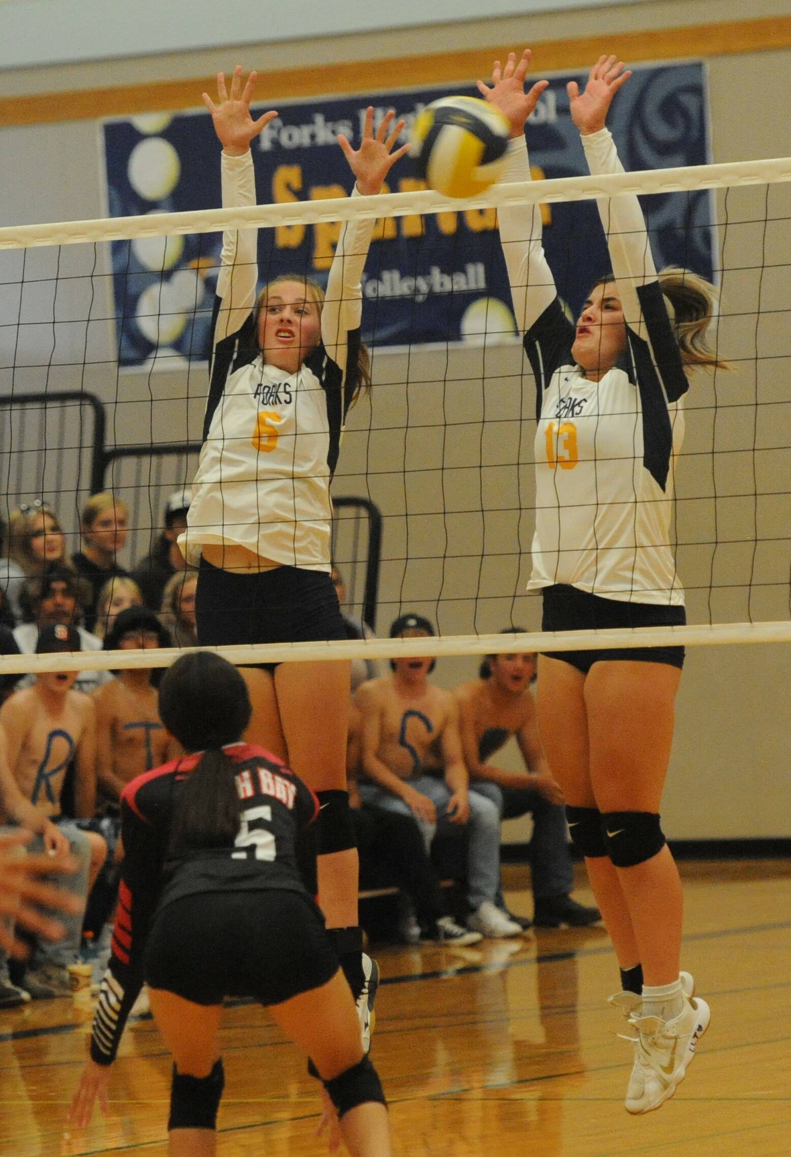 In varsity action, Spartan Chloe Gaydeski-St John (6) and Kaidence Rigby (13) go for the block while a large group of rowdy Spartan rooters look on from the stands.