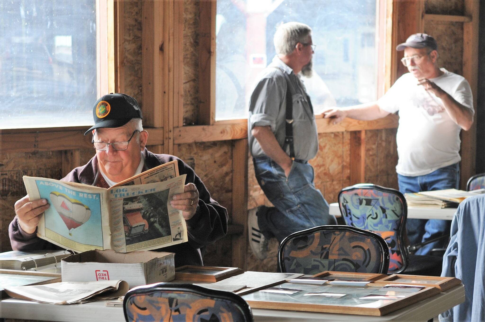 Barry Swanson reads of old-time log trucking while Joe Gaydeski and Pat Ruble share stories of the past.