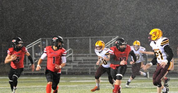 Red Devil QB Julian Carrick (5) finds running room behind the blocking of teammates Jodell Wimberly (1) and Charles Halttunen (12) during a rainy evening in Forks where Neah Bay defeated Winlock 56 to 6 earning their way into the state playoffs in 1B 8 man football. The Red Devils will face the winner of the Pomeroy/ Wellpinit game on Nov 18 or 19 with the time and place yet to be determined. Photo by Lonnie Archibald