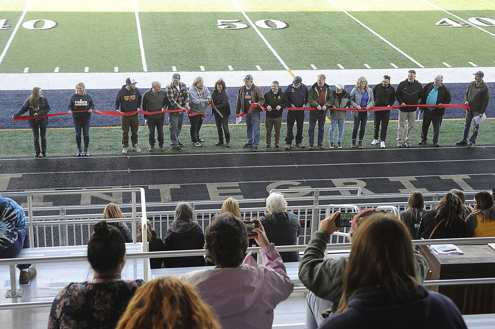 Spectators in the stands photograph the Forks Chamber of Commerce Ribbon Cutting Ceremony with cell phones during the Spartan Stadium dedication held on April 14 at the new Spartan Stadium in Forks. Photo by Lonnie Archibald