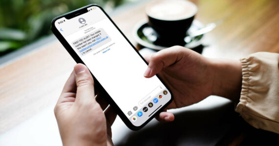 Woman sitting and holding blank screen mock up mobile phone with coffee cup at cafe.