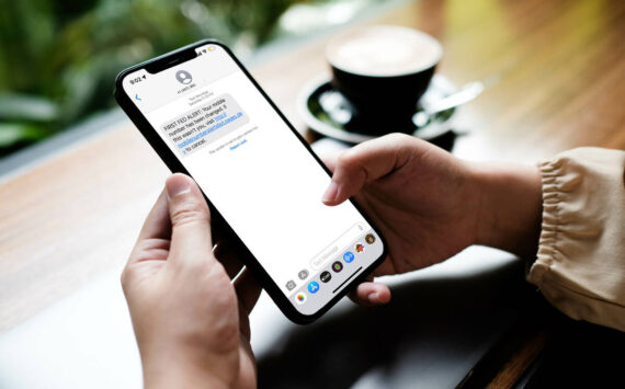 Woman sitting and holding blank screen mock up mobile phone with coffee cup at cafe.