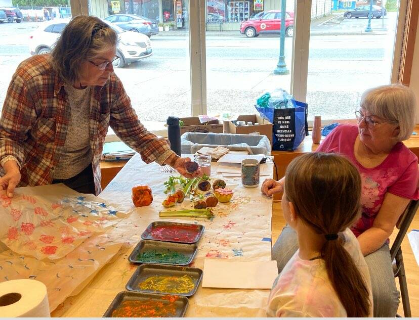 Debbie Anderson and Linda Offutt assist with a kid’s art activity of stamping with fruit at the RAC during Rainfest.