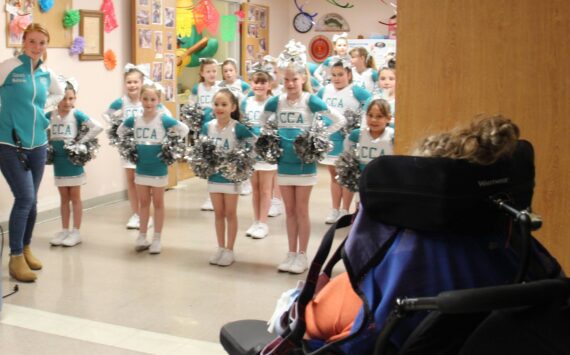 In honor of May Day members of the Coastal Cheer Academy made a visit to Forks Community Hospital Wednesday afternoon and treated the residents at LTC to some cheers and some flowers!
There are about two dozen members in CCA and they are ages seven to 13. They performed several cheers and stunts in their new uniforms and then distributed flowers to everyone. One of the coaches, Melanie Stonebreaker, seen at the left in the photo, shared that the community has given so much in getting them started that they wanted to give something back. Here a LTC resident looks on as the group gets ready to give an enthusiastic cheer! Photo Christi Baron