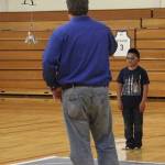 The judge films the boys team as one student directs while the other students fly the drone to the correct spot on the mat where it will drop its payload. In addition to operating their drones, each team also had to program a land rover-type vehicle that had to perform particular tasks at certain points on the mat.