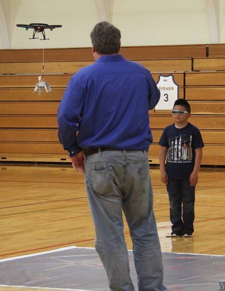The judge films the boys team as one student directs while the other students fly the drone to the correct spot on the mat where it will drop its payload. In addition to operating their drones, each team also had to program a land rover-type vehicle that had to perform particular tasks at certain points on the mat.