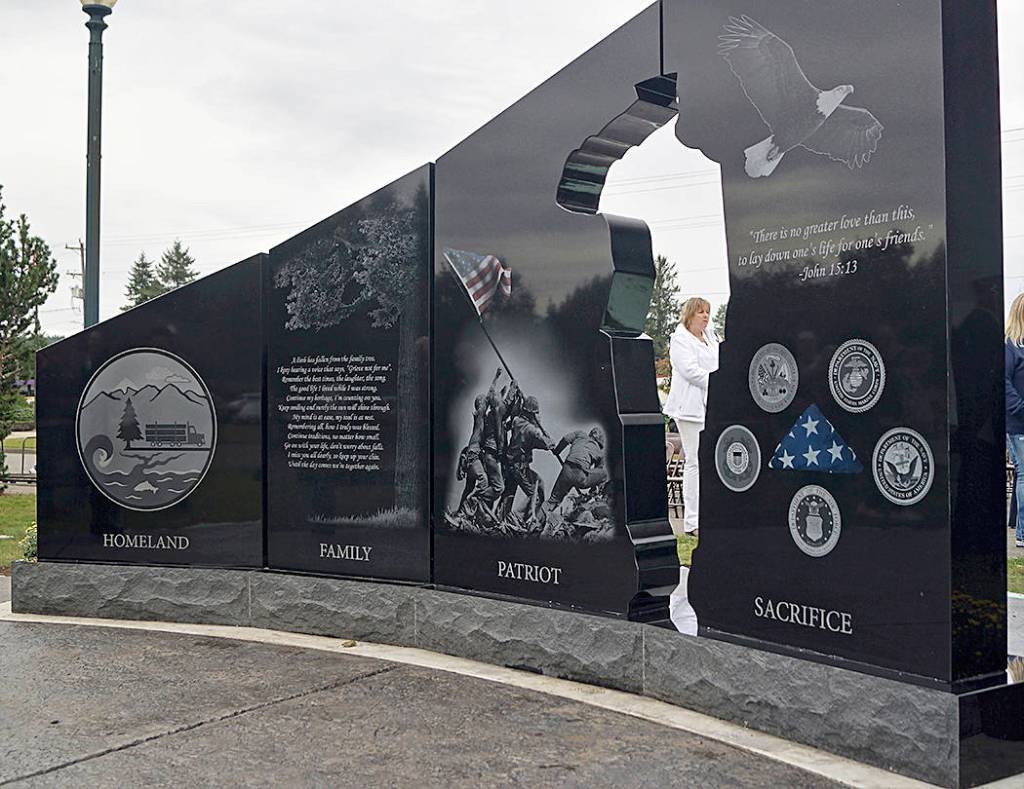 A Gold Star Mother is seen through the opening in the monument. The cut-out area in the granite is in the shape of a saluting soldier. The committee worked thoughtfully to select the items that appear on the backside of the monument to represent our community and those we have lost. Photo Vern Hestand