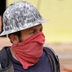 A worker wears a cloth tied around his face as a makeshift mask on a townhouse construction site Friday, April 24, 2020, in Seattle. Gov. Jay Inslee announced that some construction projects will be allowed to resume amid the coronavirus pandemic, including low-risk projects and only with physical distancing and other requirements. (Elaine Thompson/Associated Press)