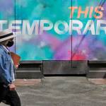 A person wearing a mask walks past a mural on a boarded-up window that reads This is temporary, on Tuesday, April 28, 2020, in Seattle. Public street art has sprung up all over the city as businesses closed to prevent the spread of the coronavirus or due to government stay-at-home orders have temporarily boarded up their windows. (Ted S. Warren/Associated Press)