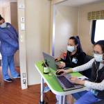 Sarah VanBuskirk, left, looks across to talk with fellow patient service specialists Yuehua Liang, right, and Eva Villanueva as they prepare records via cell phone for patients driving up to a coronavirus testing site Wednesday, April 29, 2020, in Seattle. The site, open Wednesdays and Saturdays from 10 a.m. to 3 p.m. in the Rainier Beach neighborhood, is available to anyone displaying the virus symptoms, are pregnant, over 60 or have a chronic condition, as well as health care workers and first responders. (Elaine Thompson/Associated Press)