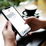 Woman sitting and holding blank screen mock up mobile phone with coffee cup at cafe.