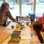 Debbie Anderson and Linda Offutt assist with a kids art activity of stamping with fruit at the RAC during Rainfest.