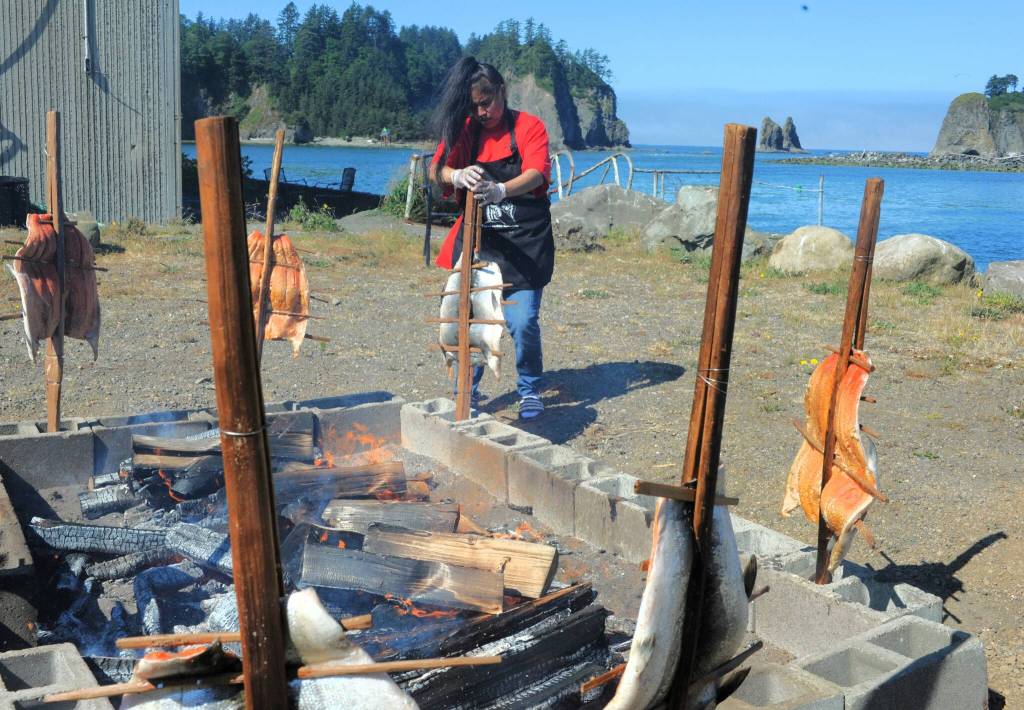 Below, Margarita Guerrero prepares baked salmon, in the traditional way, while James Island stands boldly across the Quillayute River during the Quileute Days celebration. 
Photo by Lonnie Archibald