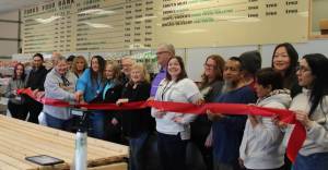 Photo by Christi Baron
Customers, board members, volunteers, staff, and more gathered last Thursday to celebrate the Forks Community Food Bank with an official Forks Chamber of Commerce ribbon-cutting ceremony. The Food Bank also welcomed the community on that day to check out all the changes and improvements that have taken place. After extensive remodeling of the former Clothing Bank area, the facility expanded and now operates more like a market where clients get what they need/prefer and not pre-selected items.
Holding the big scissors are Chamber Executive Director Lissy Andros and Sena Engeseth, Food Bank operations manager.