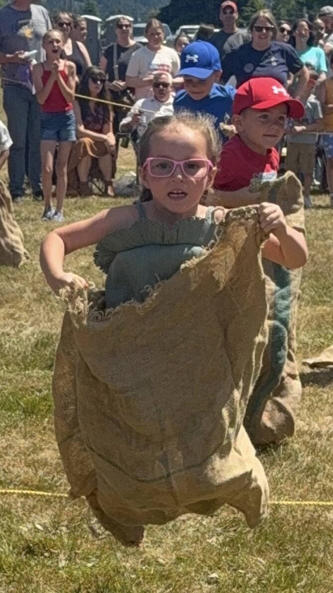 Corey Stensland, age 5, great-granddaughter of Rick and Pam Gale, with the win, in the Gunny Sack Race, Sunday in Tillicum Park. Her cousin, Aubrey Gale, can be seen in the background, cheering her on. 
Photos by Pam Gale
