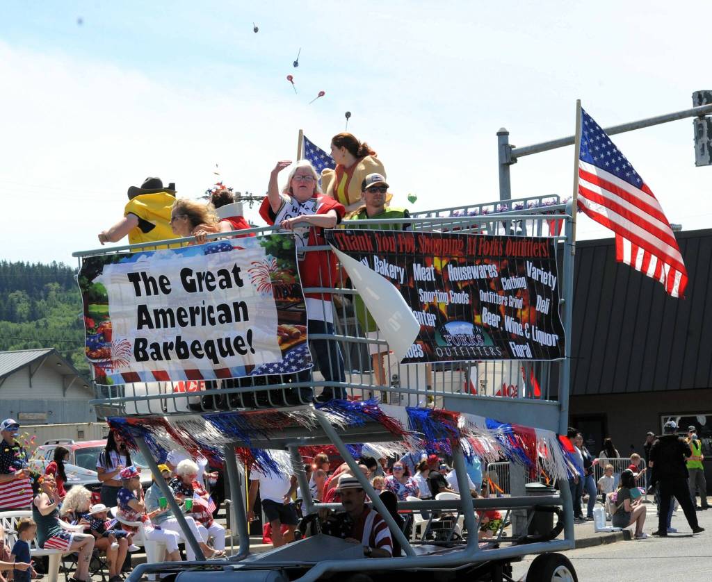 Photos by Lonnie Archibald
Above, a parade regular, the Outfitters Big Shopping Cart, featured employees dressed as backyard BBQ items. Here a bottle of Ketchup, also known as store employee Tina Matchett, throws some sweet treats to parade watchers. Store owner Bruce Paul is at the wheel below.
