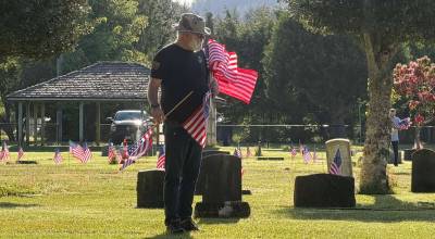 Right: Volunteer Tim Wade, with an armload of newly purchased flags, courtesy of the Forks American Legion, looks for veterans graves last week at the Forks Cemetery. 
Photo Mike Zavadlov
